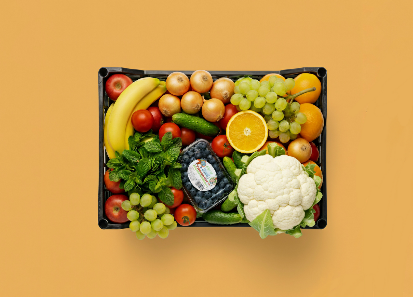Assorted fruits and vegetables in a black tray on a yellow background